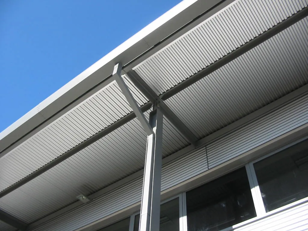 Looking up at a profiled metal canopy soffit and its steel supports against a blue sky