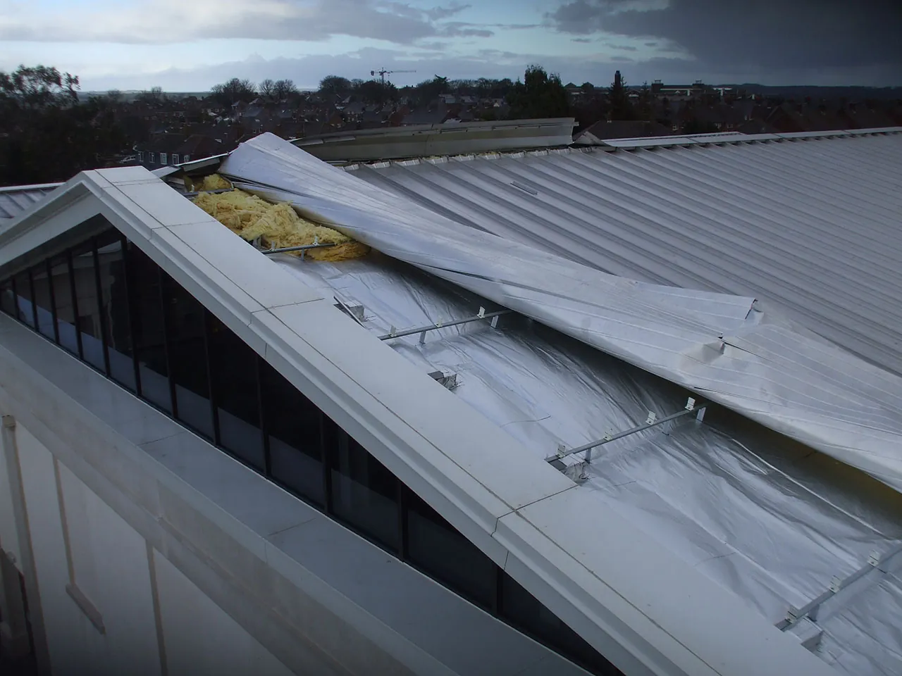 Roof sheets torn back along a ridge, exposing the insulation beneath